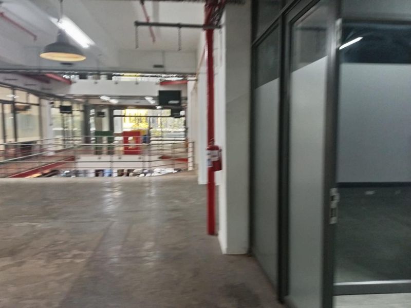 An open-plan office space featuring industrial-style exposed ceilings, fire safety infrastructure, and glass-partitioned rooms with polished concrete flooring.