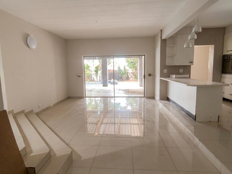 Spacious open-plan living area featuring polished tile flooring, a sunken lounge, and a modern kitchen with built-in cabinetry and island, leading to an outdoor patio.