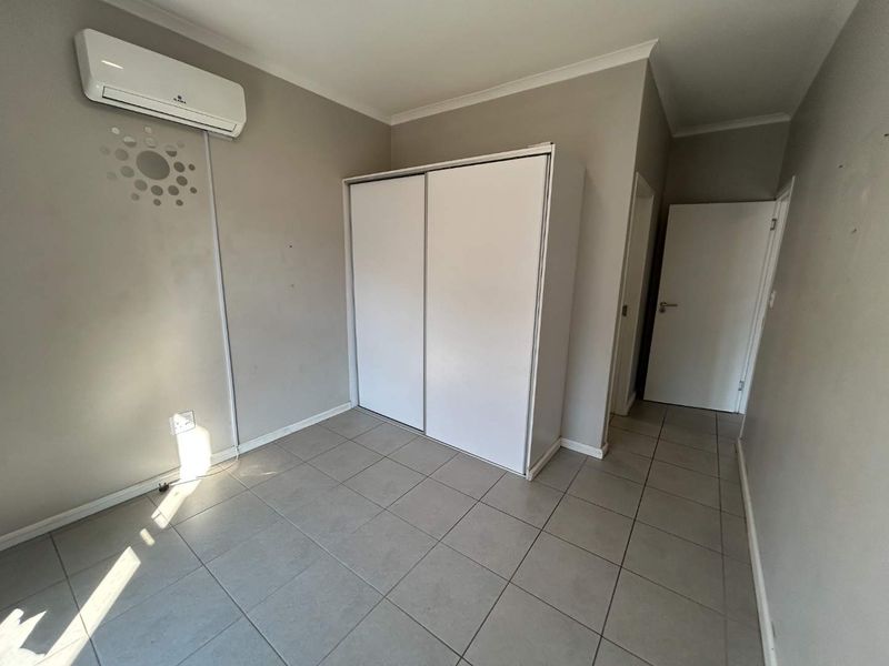 A clean, empty bedroom featuring tiled flooring, a built-in wardrobe, and a wall-mounted split-system air conditioning unit.