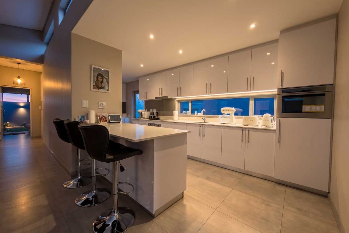 Modern kitchen featuring sleek white cabinetry, quartz countertops, a central island with breakfast bar seating, and integrated appliances with ambient under-cabinet lighting.