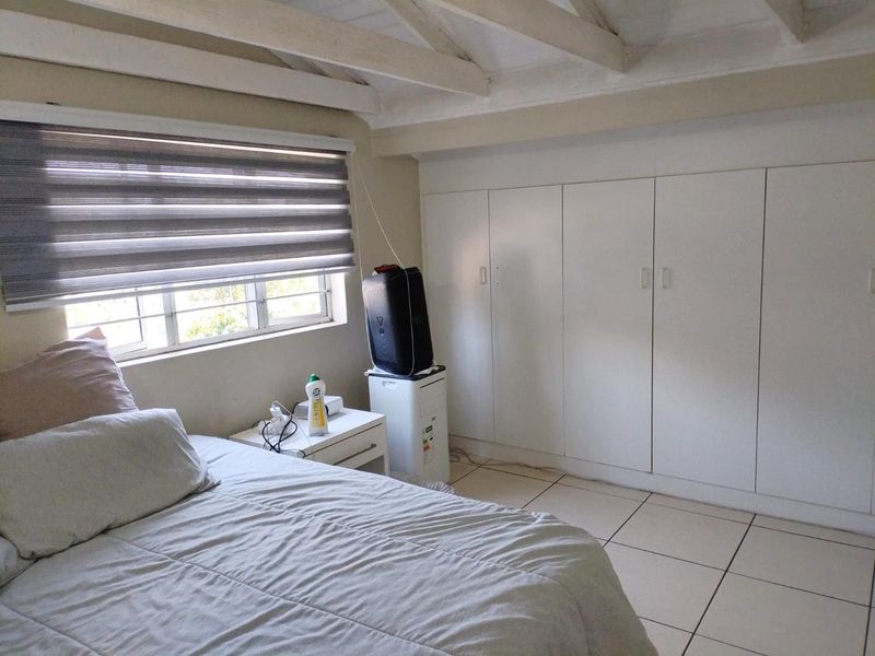 A bedroom featuring built-in cupboards, tiled flooring, and exposed timber ceiling beams, providing a functional space with natural light.