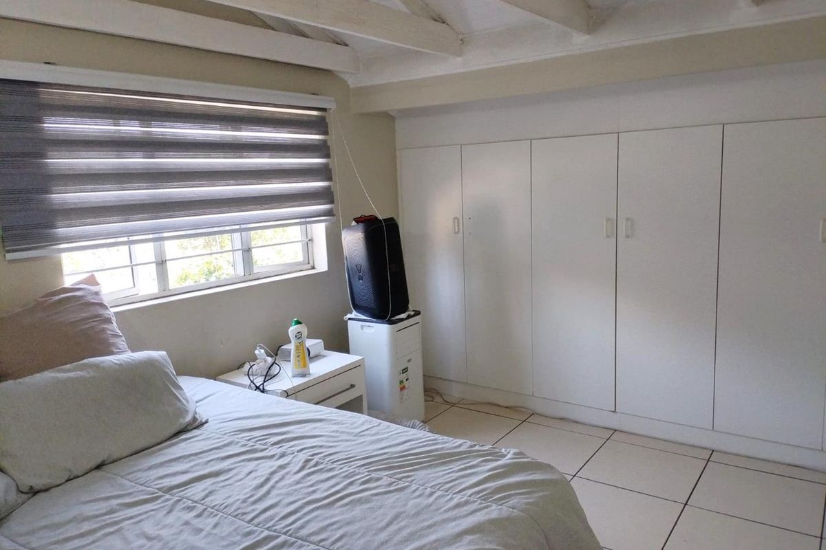 A bedroom featuring built-in cupboards, tiled flooring, and exposed timber ceiling beams, providing a functional space with natural light.