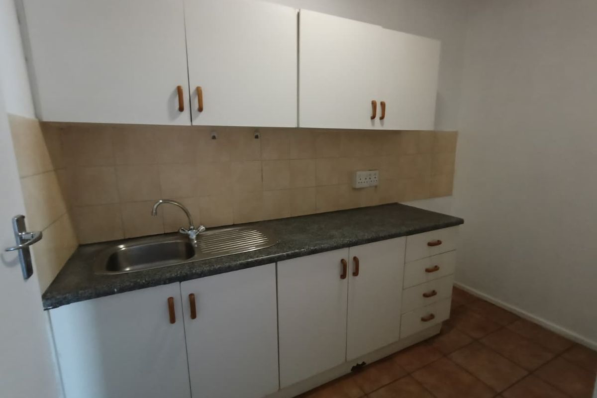 A compact kitchen area featuring white cabinetry, laminate countertops, a stainless steel sink, and tiled backsplash, offering a functional space for basic utility needs.
