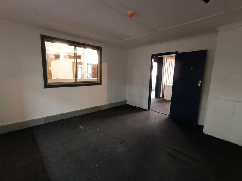 An empty office space featuring dark carpeting, a sliding window, and a doorway leading to an adjacent area.