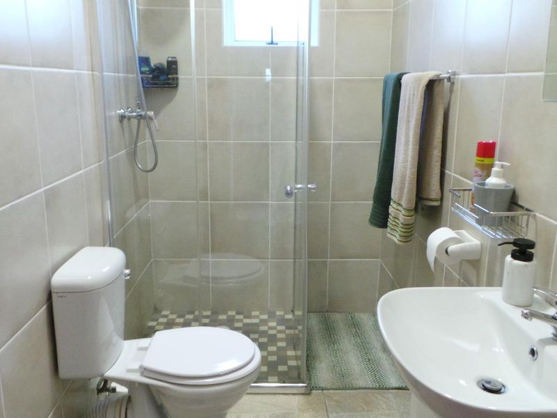 A functional bathroom featuring a glass-enclosed shower, pedestal basin with chrome mixer tap, and neutral ceramic wall tiling.