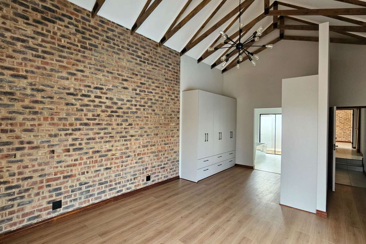 Spacious bedroom featuring a vaulted ceiling with exposed timber trusses, a striking exposed brick feature wall, and built-in cabinetry.
