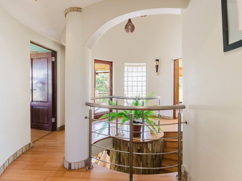 A bright landing area featuring a curved staircase with a modern stainless steel balustrade, wooden flooring, and a unique glass block window feature.