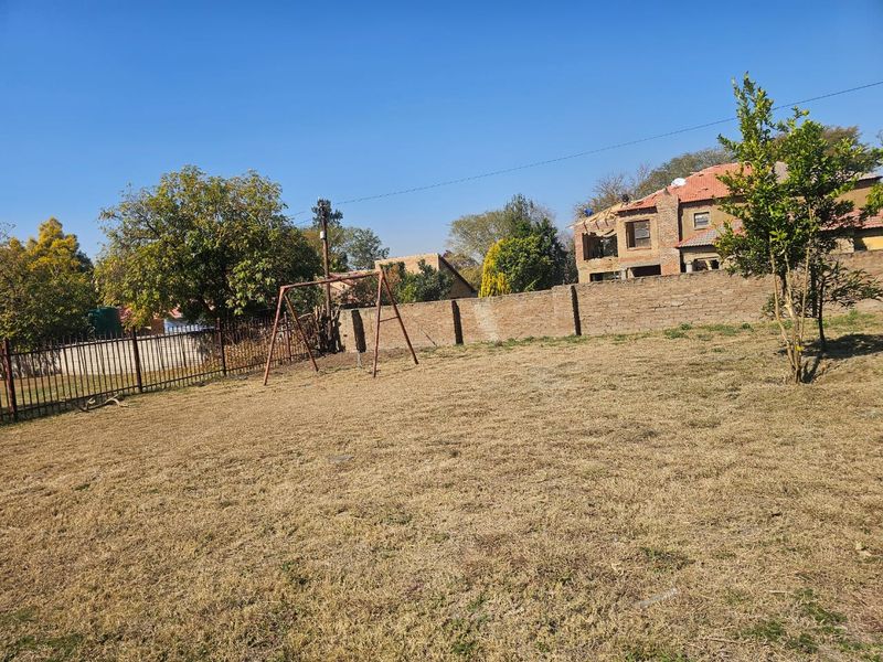 A spacious, open garden area featuring a brick boundary wall and metal perimeter fencing, offering potential for landscaping and outdoor development.