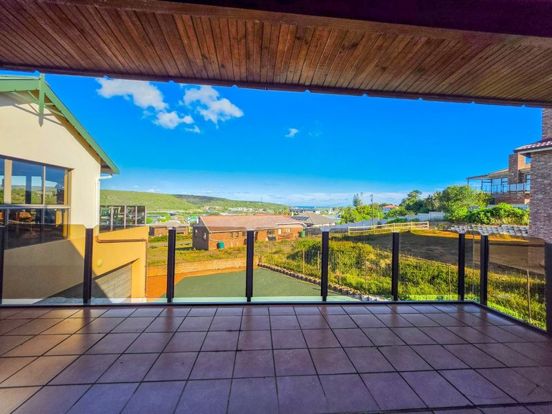 A spacious covered balcony featuring tiled flooring, a timber ceiling, and a modern glass balustrade, offering expansive views of the surrounding landscape.