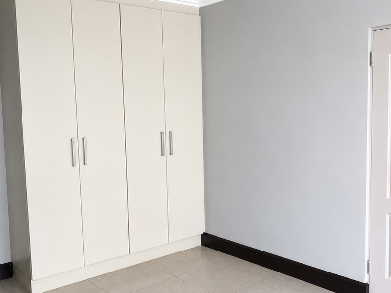 A clean, empty bedroom featuring neutral tiled flooring, built-in cupboards, and modern grey wall finishes.