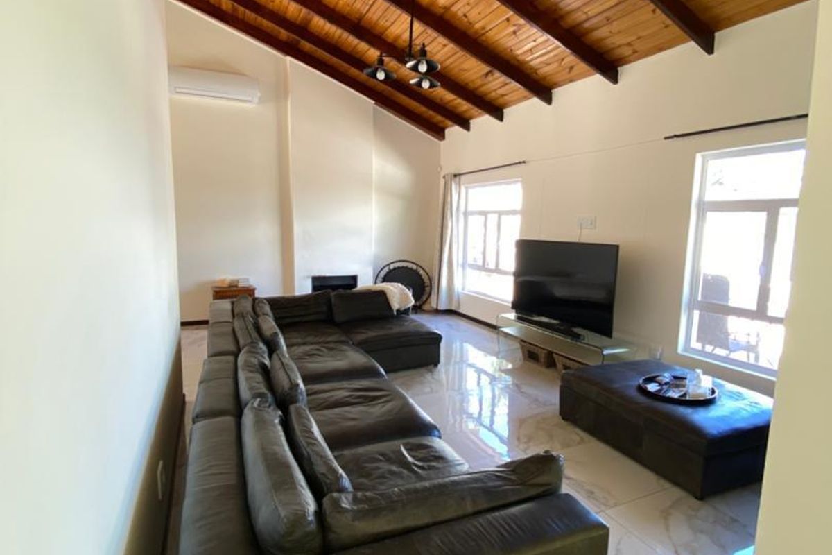 Spacious living room featuring high vaulted timber ceilings, polished marble-look floor tiles, and a built-in fireplace, creating a bright and airy atmosphere.