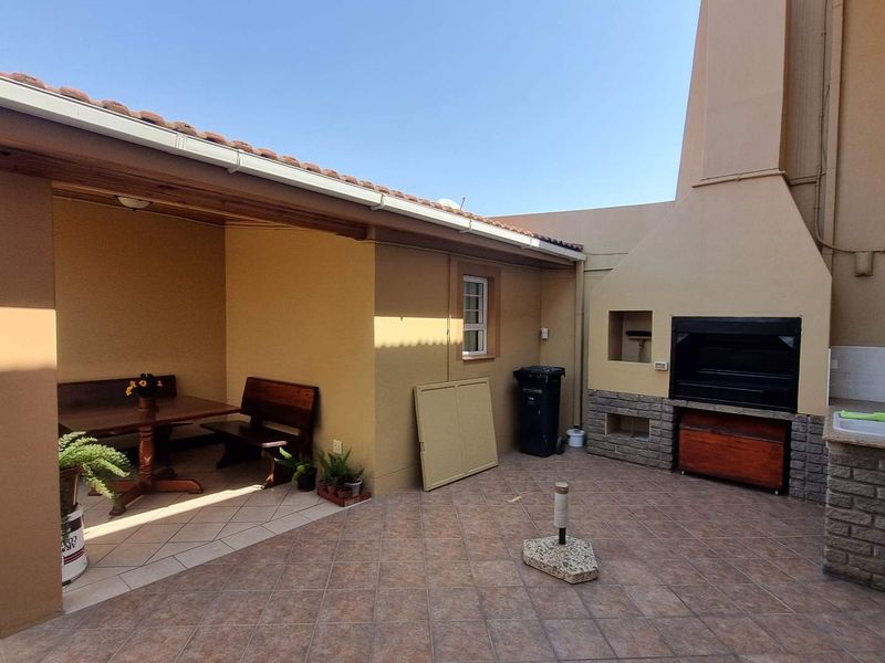 Covered outdoor patio area featuring a built-in braai, brickwork detailing, and an integrated sink, providing a functional space for outdoor entertaining.