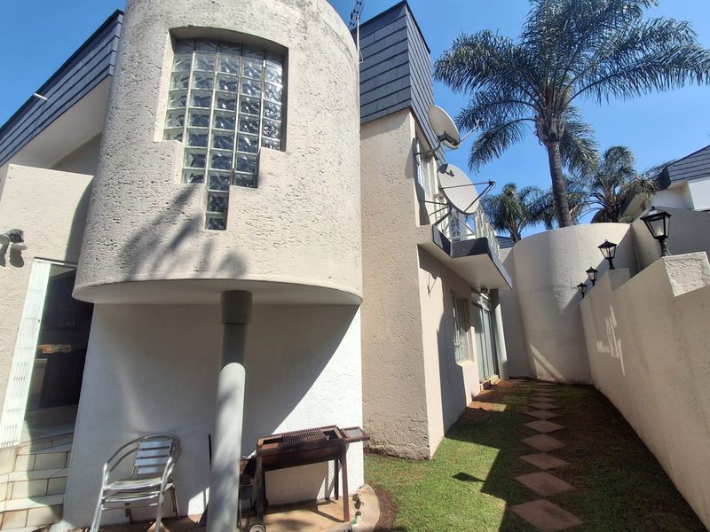 Rear exterior view of the townhouse featuring a unique curved architectural design, glass block window, paved garden path, and exterior wall lighting.