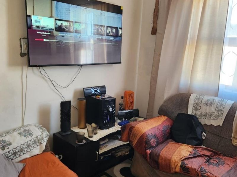 A living room area featuring a wall-mounted television and window with curtain rail, showing signs of wear on the wall surfaces.
