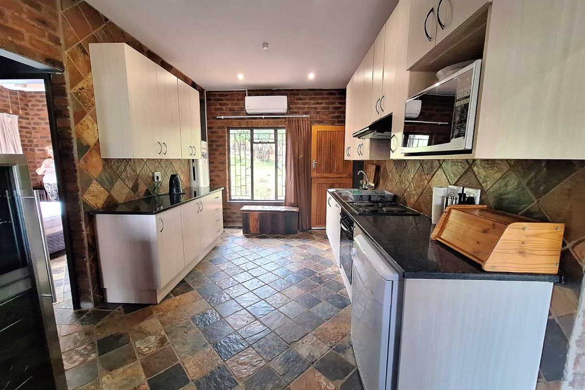 A functional kitchen featuring light-toned cabinetry, dark granite countertops, built-in oven and hob, and distinctive slate-style floor and wall tiling.
