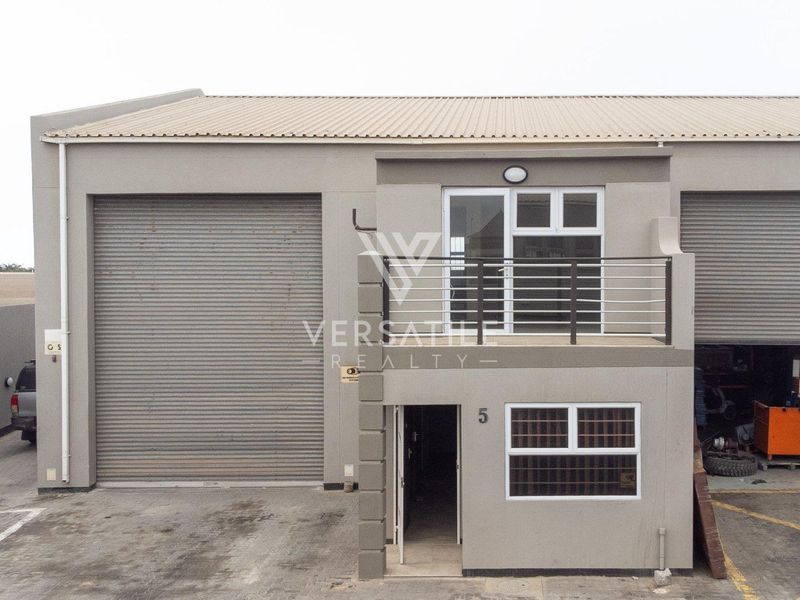 Industrial unit featuring a large roller shutter door, ground floor entrance, and an upper-level balcony with metal railings.