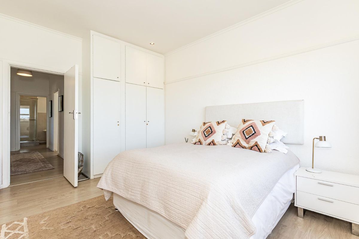 A bright bedroom featuring built-in floor-to-ceiling cabinetry and light-toned flooring, with an adjacent view into a bathroom area.