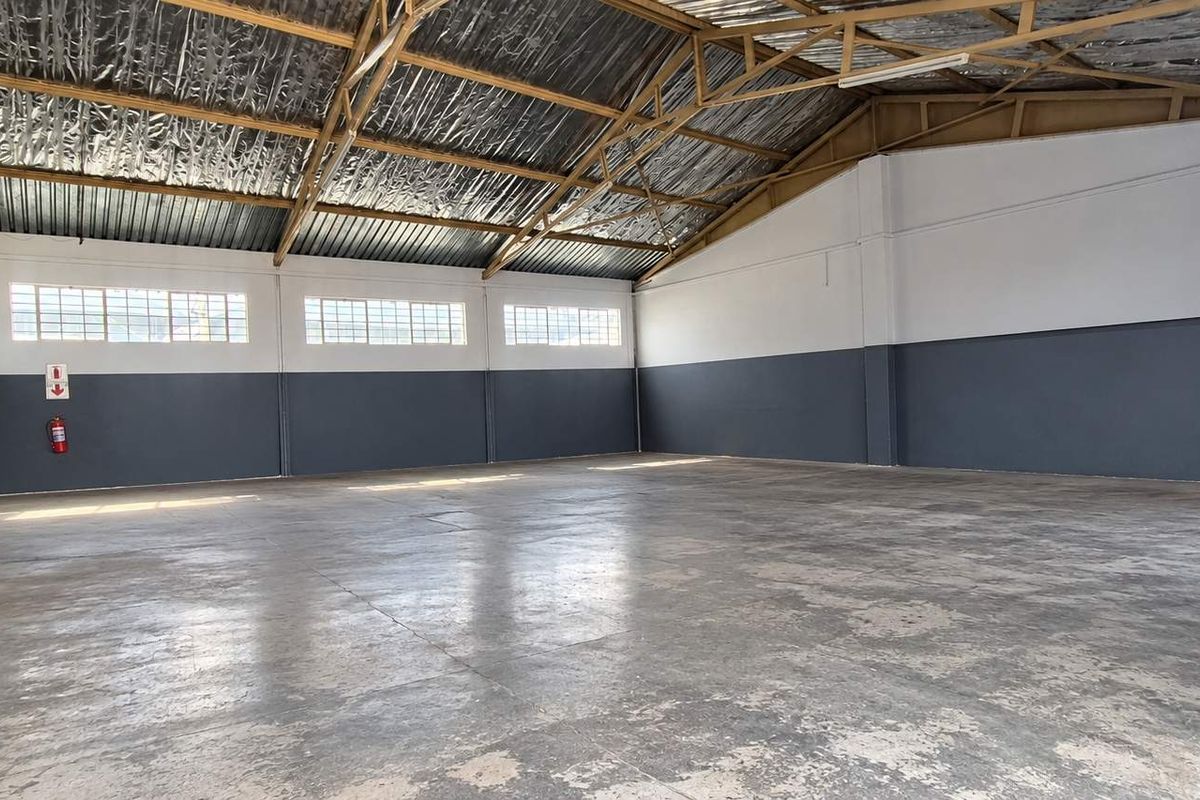 Spacious industrial warehouse unit featuring high exposed steel roof trusses, durable concrete flooring, and ample natural light through industrial-style windows.
