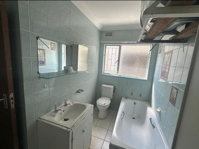 A dated bathroom featuring full-height wall tiling, a built-in vanity, a standard bathtub, and a toilet, requiring cosmetic updates to modernize the space.