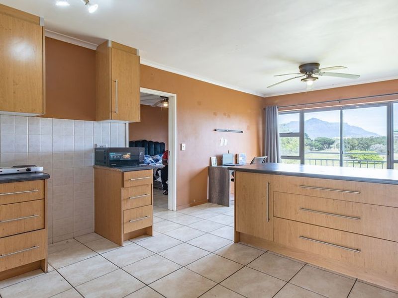 Open-plan kitchen and living area featuring light wood cabinetry, tiled flooring, and a sliding door leading to a balcony with scenic mountain views.