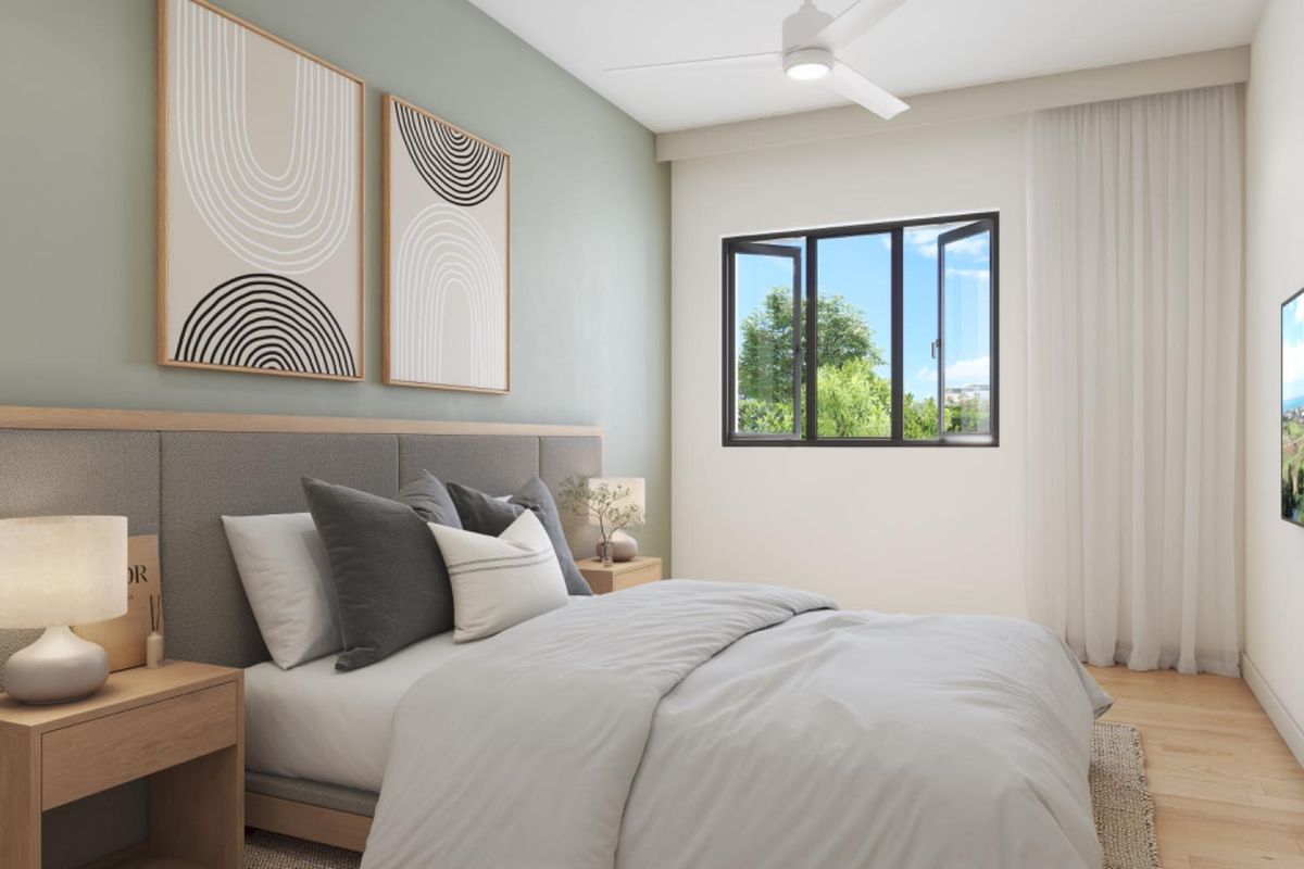 A modern, well-lit bedroom featuring a built-in upholstered headboard, ceiling fan, and large window with natural light.