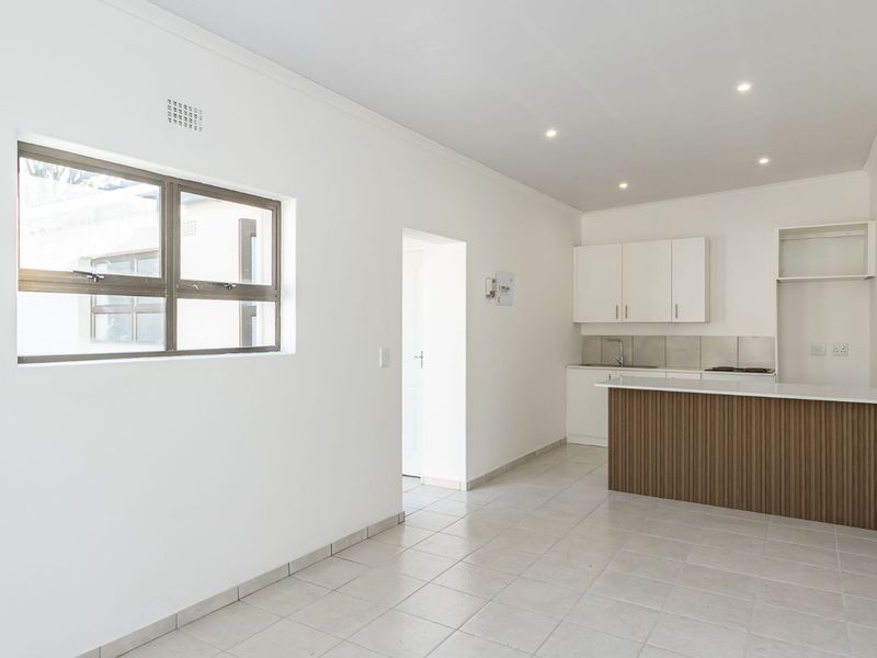 An open-plan living and kitchen area featuring tiled flooring, recessed lighting, and a modern kitchen island with built-in cabinetry.