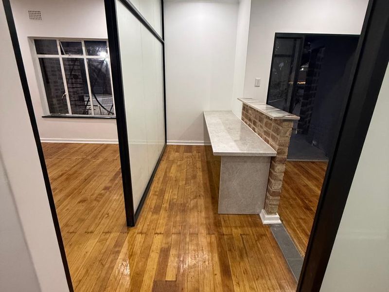 Modern office space featuring polished hardwood flooring, a sleek glass partition, and a stone-topped service counter with an exposed brick accent.