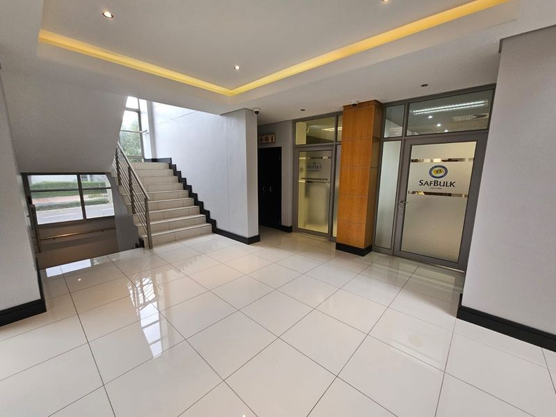 Modern office building entrance lobby featuring polished tiled floors, a central staircase, and glass-partitioned office suites with professional lighting.