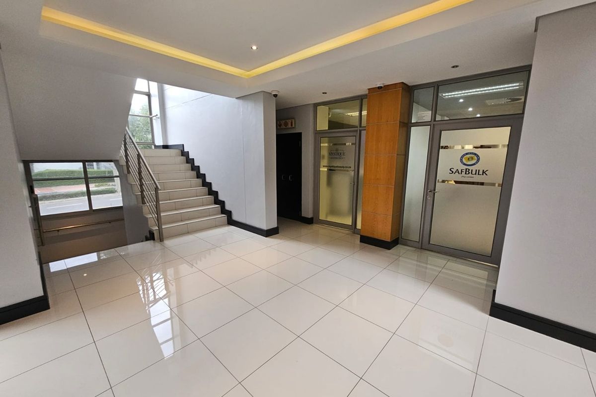 Modern office building entrance lobby featuring polished tiled floors, a central staircase, and glass-partitioned office suites with professional lighting.