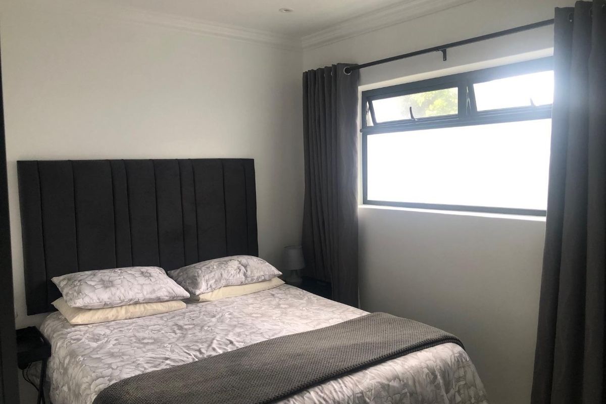 A well-maintained bedroom featuring neutral walls, crown molding, and a horizontal window with dark curtains.