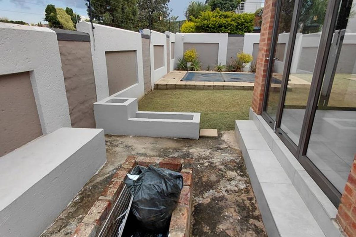 Rear garden area featuring a small lawn, perimeter walling with electric fencing, and a built-in brick braai area adjacent to the main living space.