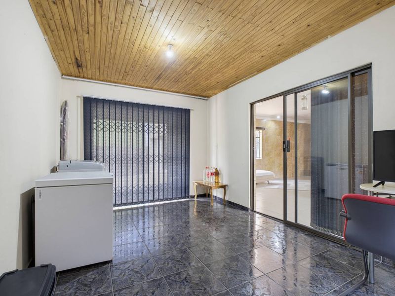 A spacious living area featuring a timber-clad ceiling, dark tiled flooring, and a sliding glass door providing access to the adjacent room.