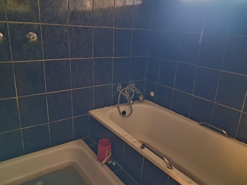 A dated bathroom featuring a built-in bathtub with wall-mounted fixtures and dark blue ceramic wall tiling, requiring renovation and modernization.
