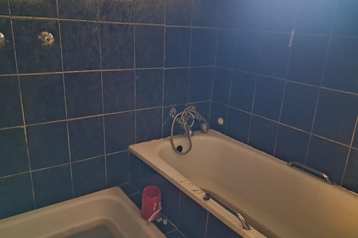 A dated bathroom featuring a built-in bathtub with wall-mounted fixtures and dark blue ceramic wall tiling, requiring renovation and modernization.