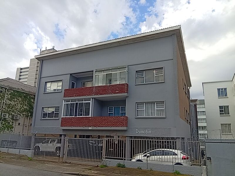 Front elevation of the Dunedin apartment building featuring a secure ground-level parking area, brick-accented balconies, and aluminium-framed windows.