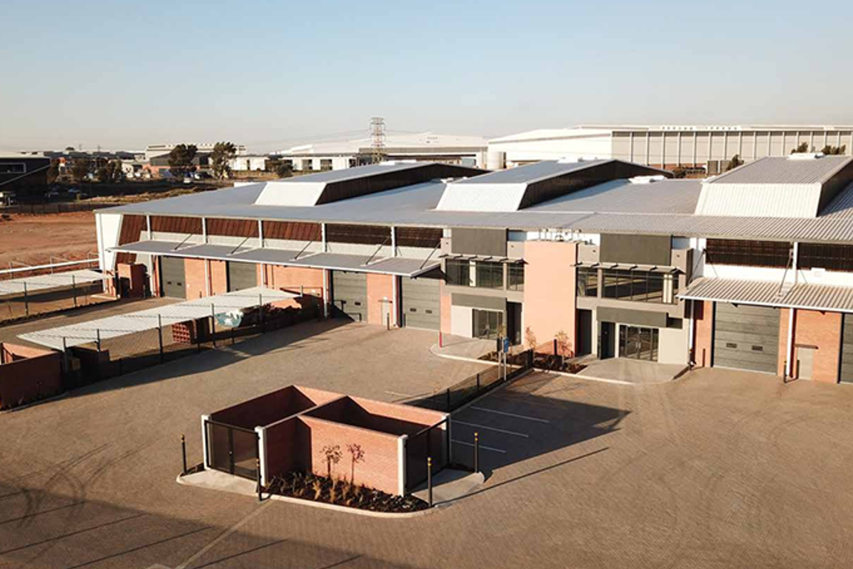 Aerial view of a modern industrial warehouse complex featuring multiple roller shutter doors, paved yard area, and secure perimeter fencing.