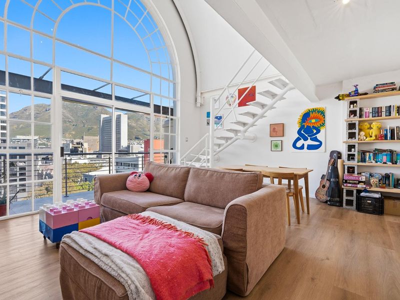Spacious living area featuring a striking arched window, modern metal staircase, and access to a balcony with scenic mountain and city views.