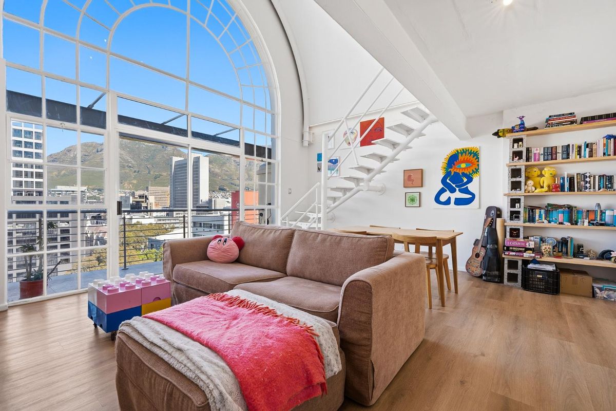 Spacious living area featuring a striking arched window, modern metal staircase, and access to a balcony with scenic mountain and city views.