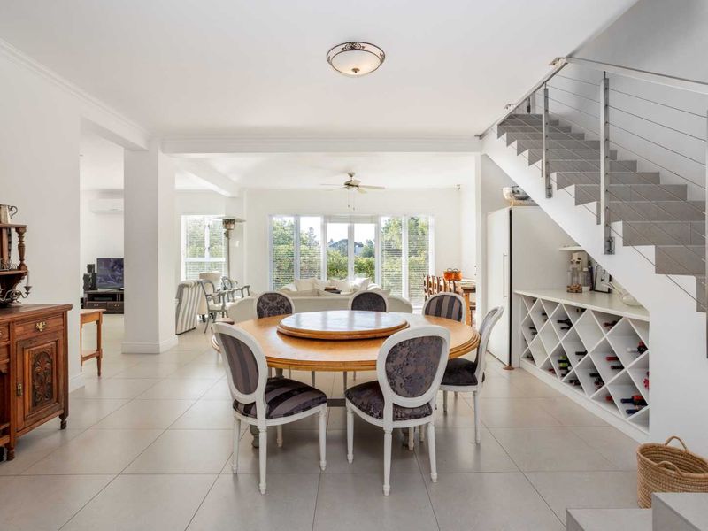 Spacious open-plan living and dining area featuring tiled floors, a modern staircase with cable railing, and a built-in wine storage unit under the stairs.