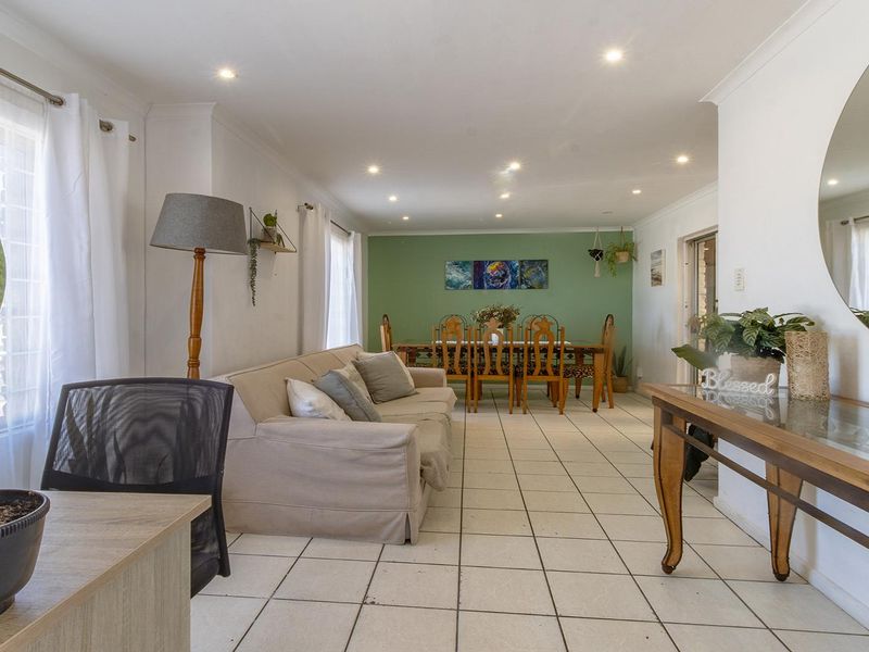 Spacious open-plan living and dining area featuring neutral tiled flooring, recessed downlighting, and a feature wall, creating a bright and versatile living space.