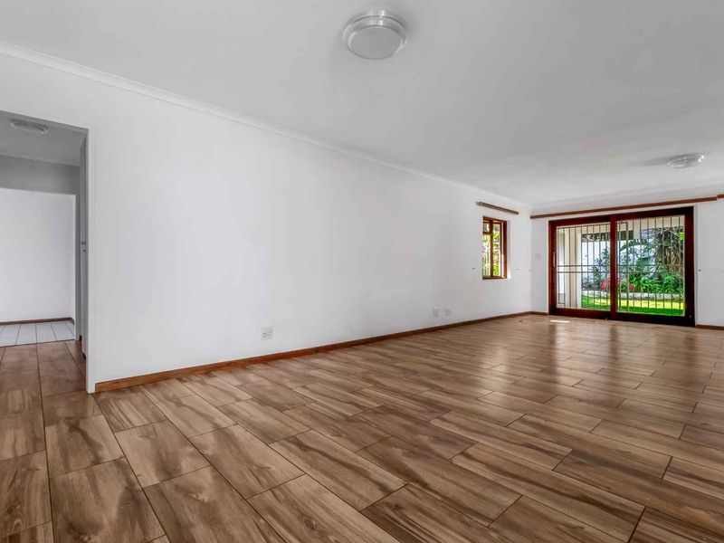 Spacious, empty living area featuring wood-look tile flooring, neutral walls, and a sliding glass door providing access to the garden.