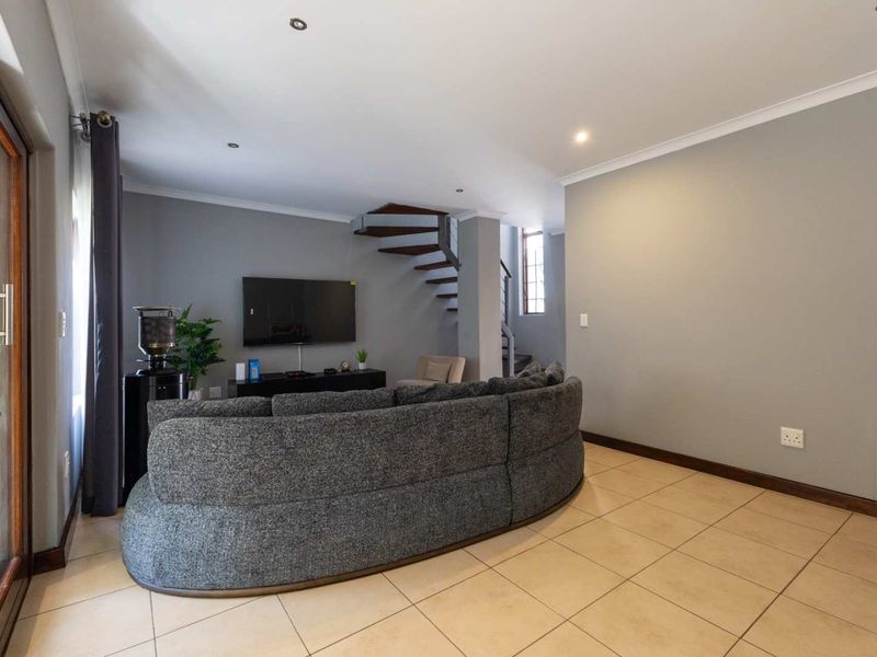 A spacious living room featuring neutral tiled flooring, recessed downlighting, and a distinctive spiral staircase leading to the upper level.
