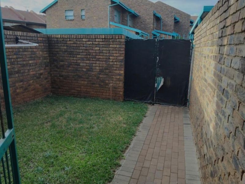 A private rear courtyard area featuring a paved walkway, small lawn, and brick boundary walls.