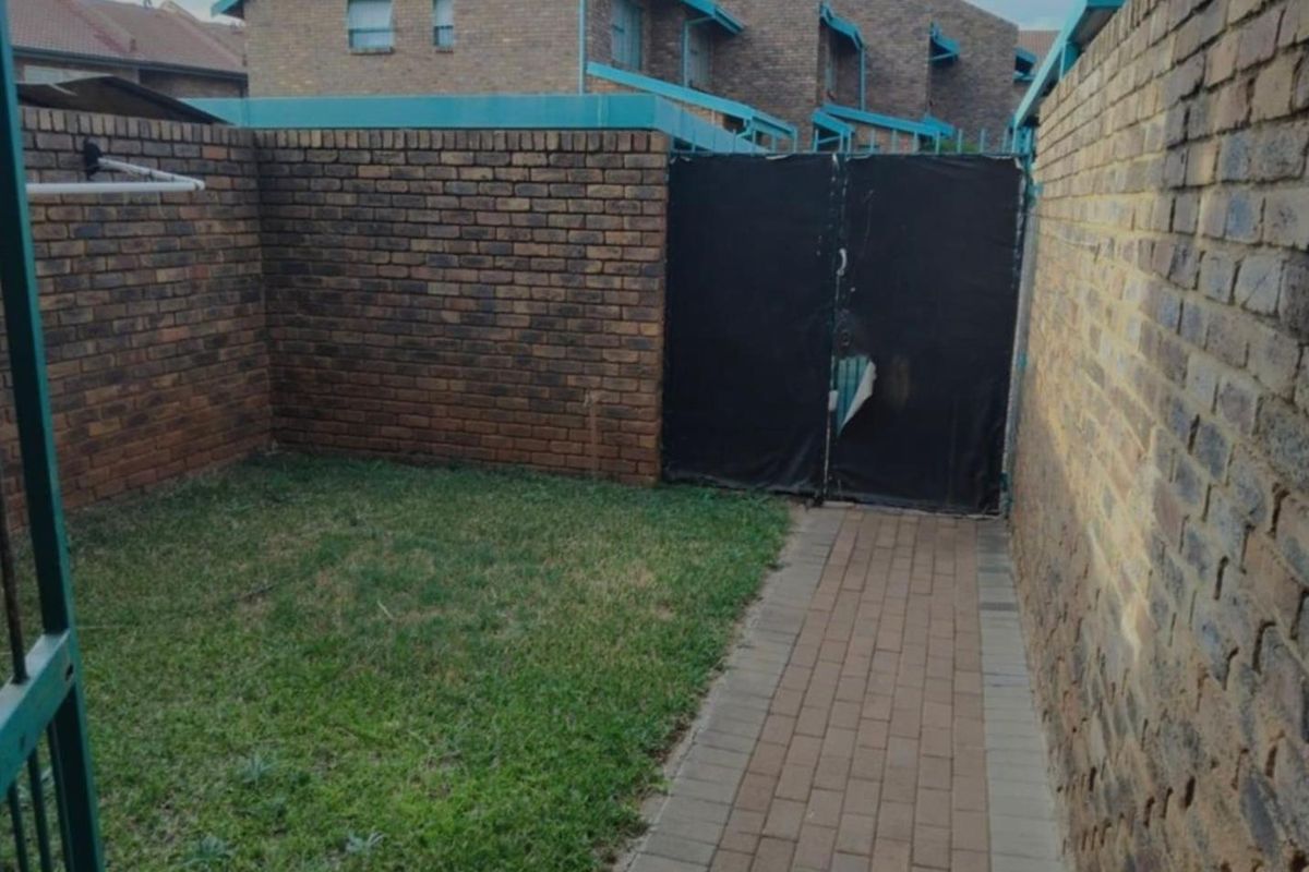 A private rear courtyard area featuring a paved walkway, small lawn, and brick boundary walls.