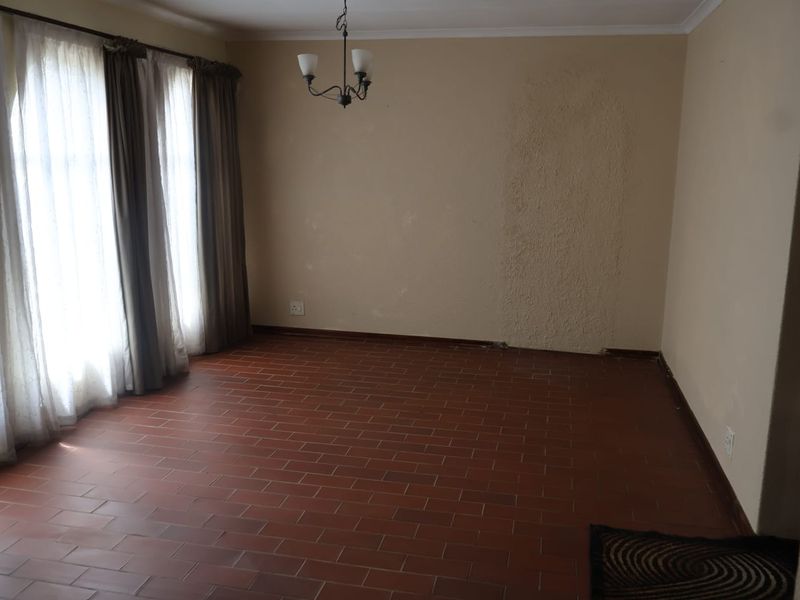 An empty living room featuring terracotta tile flooring and a central light fixture, requiring cosmetic wall repairs and updates.