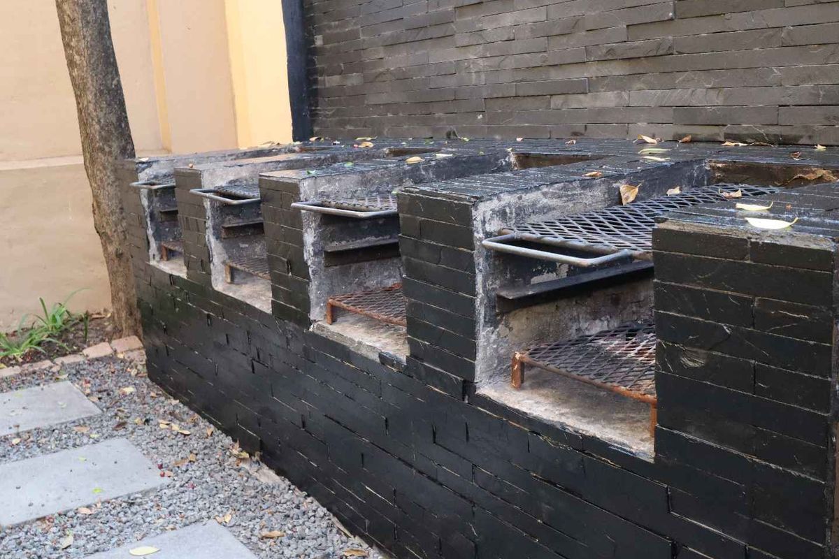 A built-in outdoor brick barbecue station featuring multiple grill sections and dark stone cladding, situated in a rear garden area.