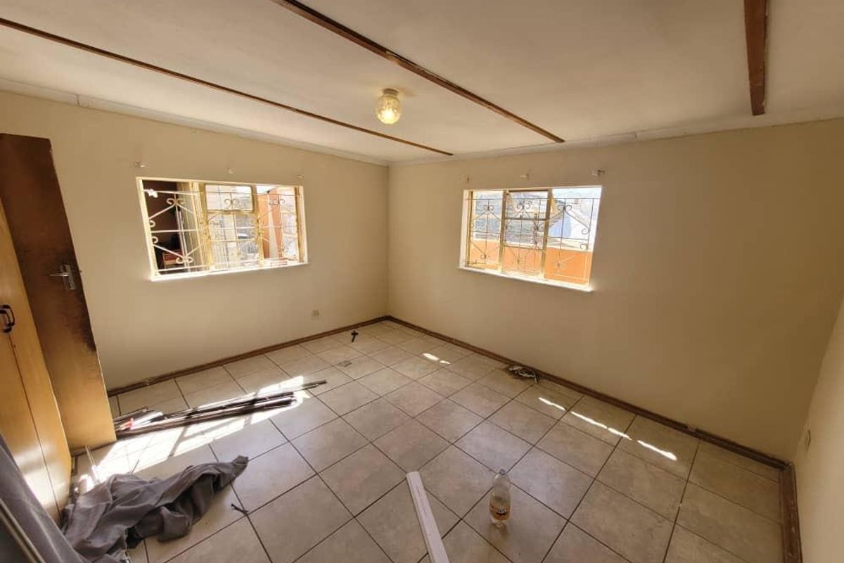 An empty bedroom featuring tiled flooring, security bars on the windows, and built-in cupboard storage, ready for renovation or staging.