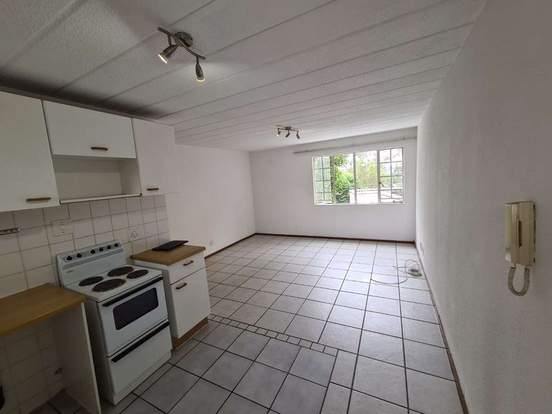 An open-plan living and kitchen area featuring tiled flooring, built-in cabinetry, and a freestanding electric stove in a clean, vacant space.