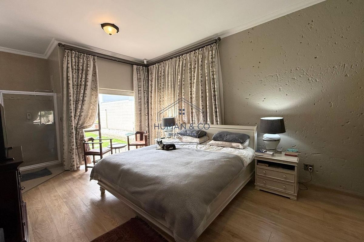 A bedroom featuring wood-look flooring, a textured accent wall, and large windows with curtains providing access to the outdoor area.