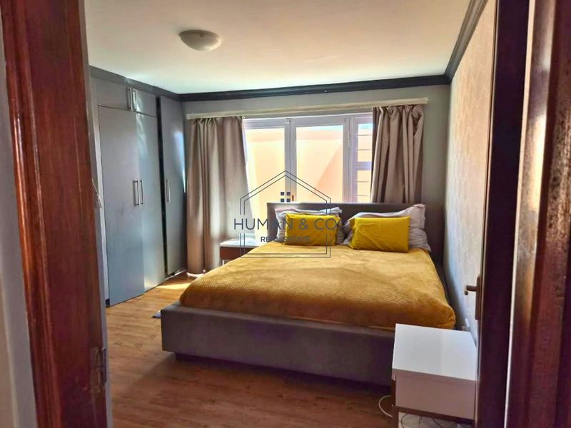 A bedroom featuring laminate flooring, built-in cupboards, and a window with curtains.